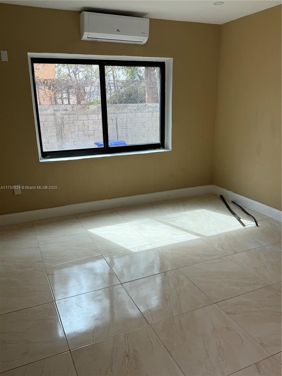 An empty room features beige walls, light-colored tile flooring, a window, and a wall-mounted air conditioner — 5501 NW Miami Ct, Miami FL 33127, MIAMI, FL
