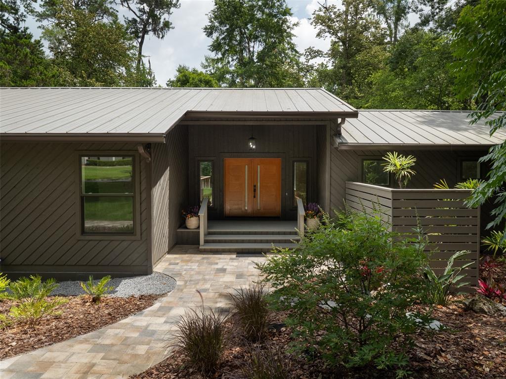 A modern house exterior features a metal roof, diagonal wood siding, and double wooden doors — 3104 NW 21ST AVENUE, GAINESVILLE, FL