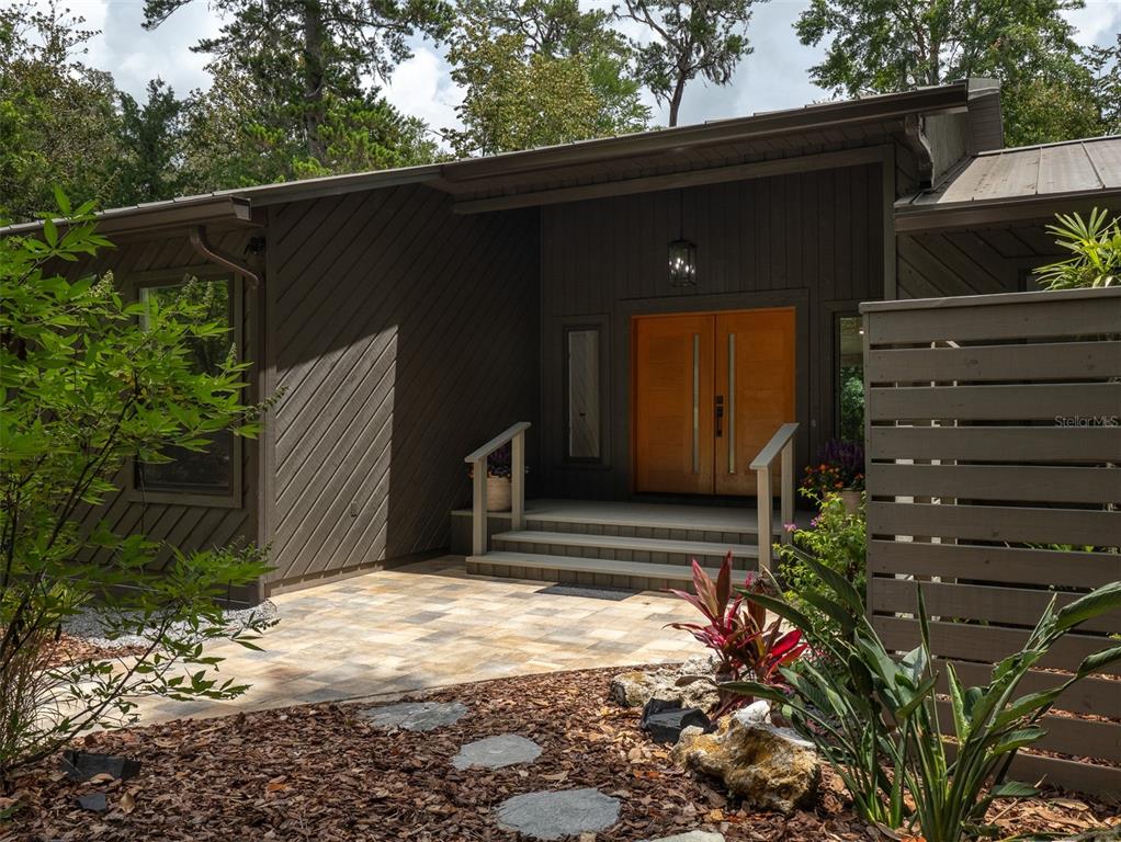 A modern home exterior features a dark wood facade, double front doors, and stone patio — 3104 NW 21ST AVENUE, GAINESVILLE, FL