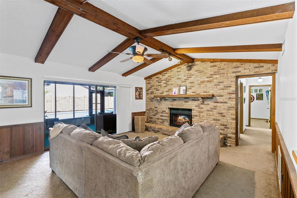 A living room features a brick fireplace, exposed wooden ceiling beams, and a sliding glass door — 120 TRAFALGAR PLACE, LONGWOOD, FL