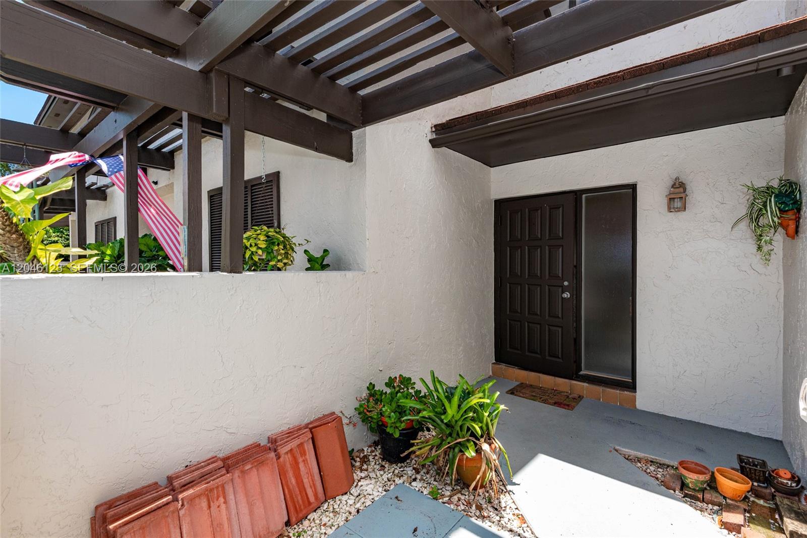 A covered entryway features a dark brown door, a pergola, and several potted plants — 8890 SW 133rd Pl # A, Miami FL 33186, MIAMI, FL