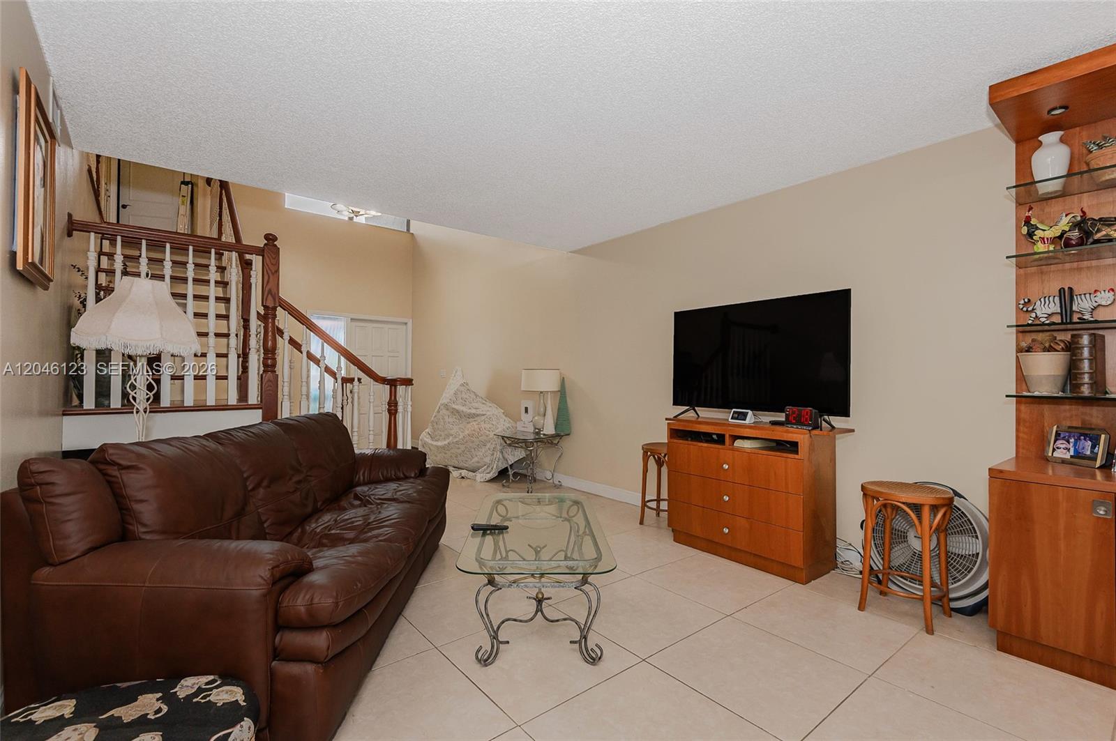 A living room features a brown leather sofa, a television on a wooden stand, and stairs — 8890 SW 133rd Pl # A, Miami FL 33186, MIAMI, FL