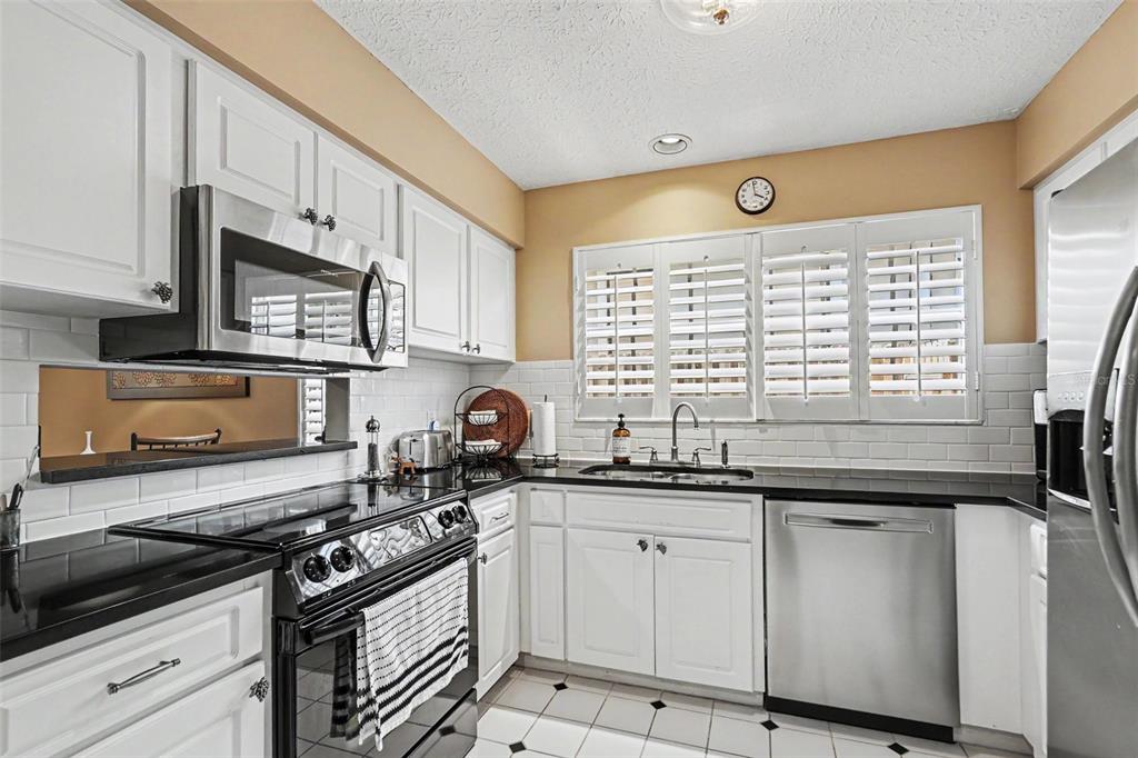 A kitchen features white cabinets, black countertops, stainless steel appliances, and white subway tile backsplash — 3053 S CONCORDIA AVENUE UNIT A, TAMPA, FL