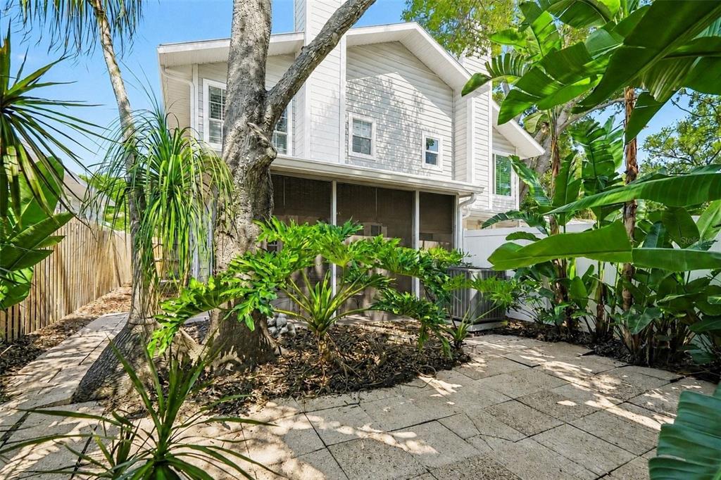 A backyard patio with stone pavers, lush tropical plants, and a screened-in porch area — 3053 S CONCORDIA AVENUE UNIT A, TAMPA, FL