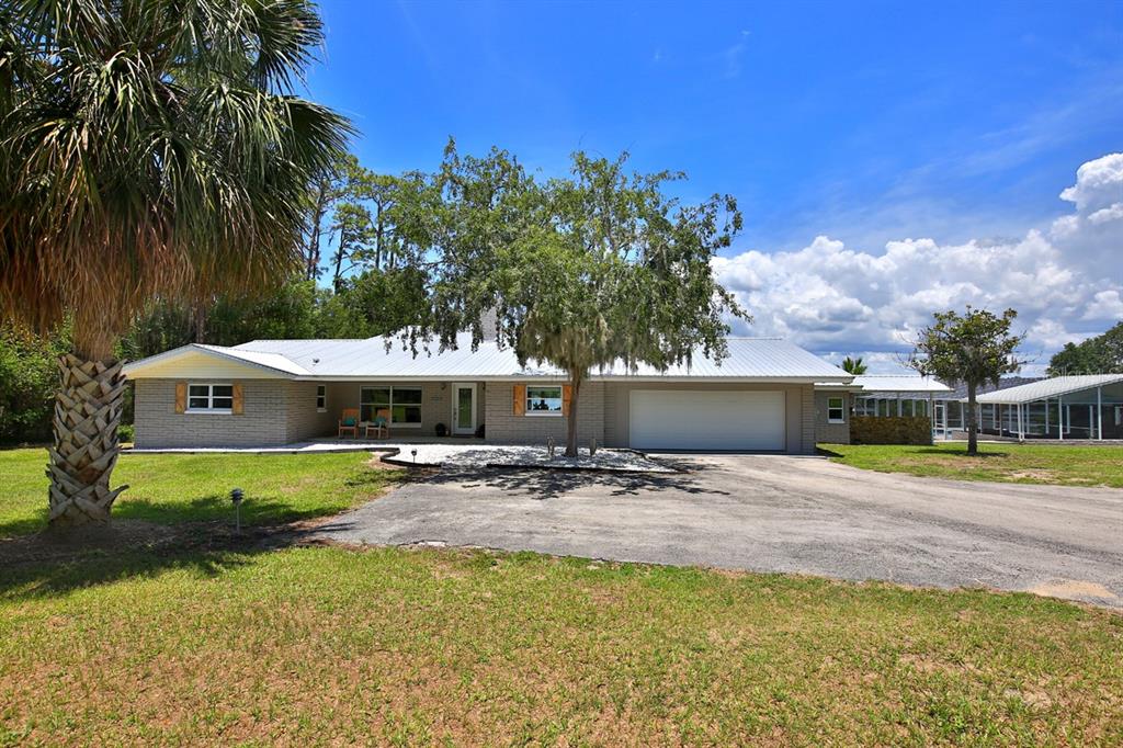 A single-story brick house with a metal roof, attached garage, and a large front yard — 10893 SE 141 AVENUE ROAD, OCKLAWAHA, FL