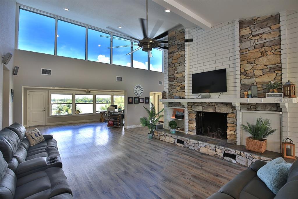 A living room features a stone fireplace, vaulted ceilings, large windows, and wood-look flooring — 10893 SE 141 AVENUE ROAD, OCKLAWAHA, FL