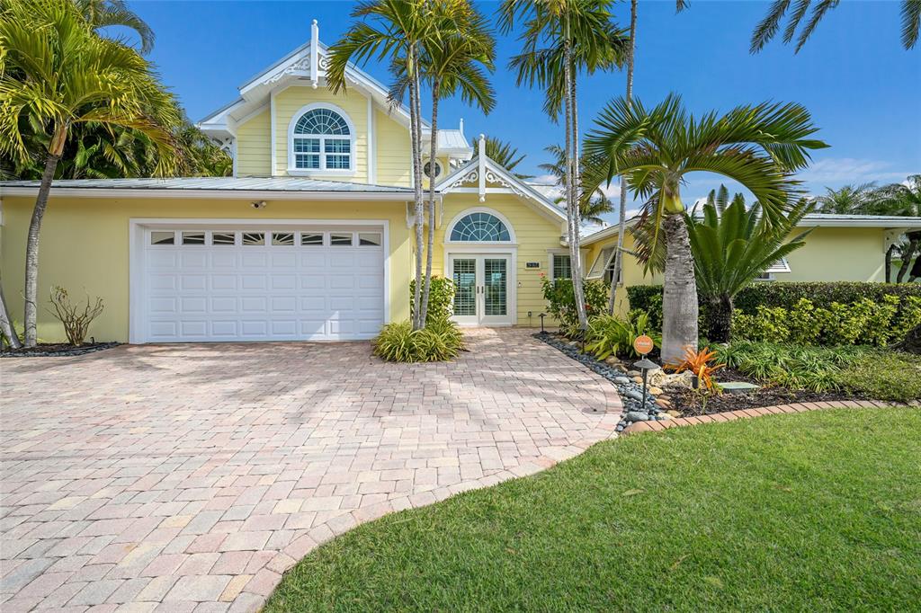 A yellow two-story house with a white garage and a paved driveway under palm trees — 8321 MARINA DRIVE, HOLMES BEACH, FL