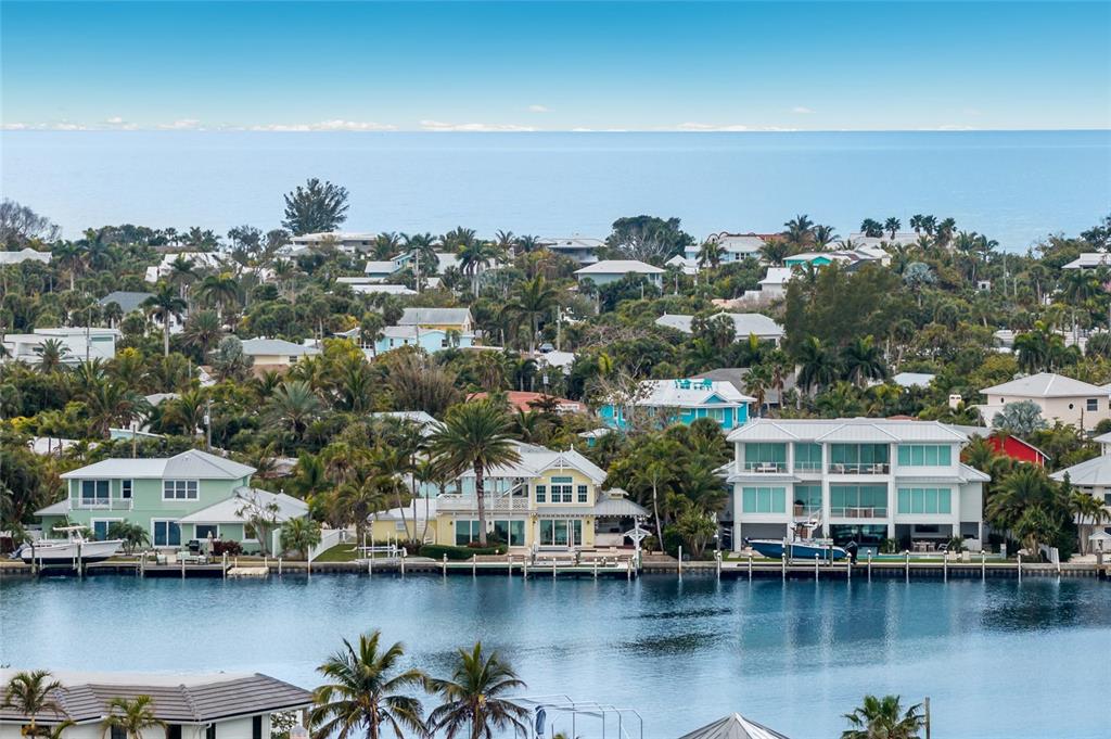 An aerial view shows waterfront houses with boat docks along a canal near the ocean — 8321 MARINA DRIVE, HOLMES BEACH, FL