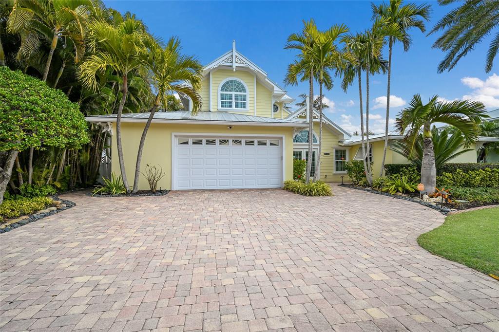 A yellow two-story house with a paved driveway and palm trees under a blue sky — 8321 MARINA DRIVE, HOLMES BEACH, FL