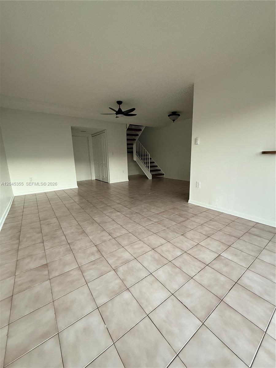 An open living area features light-colored tile flooring and a staircase with a white railing — 9390 W Flagler St # 224C, Miami FL 33174, MIAMI, FL