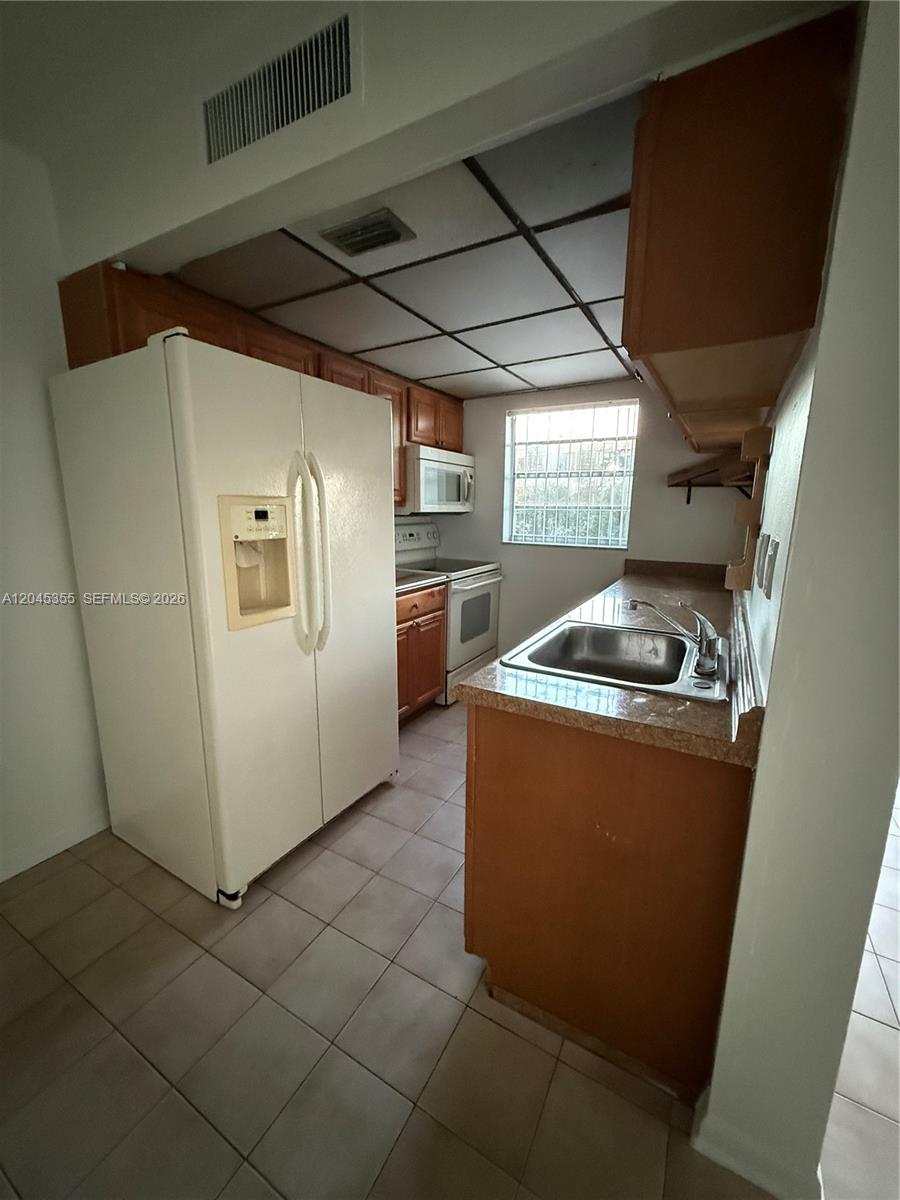 A galley-style kitchen features wood cabinets, white appliances, a drop-in sink, and a tiled ceiling — 9390 W Flagler St # 224C, Miami FL 33174, MIAMI, FL