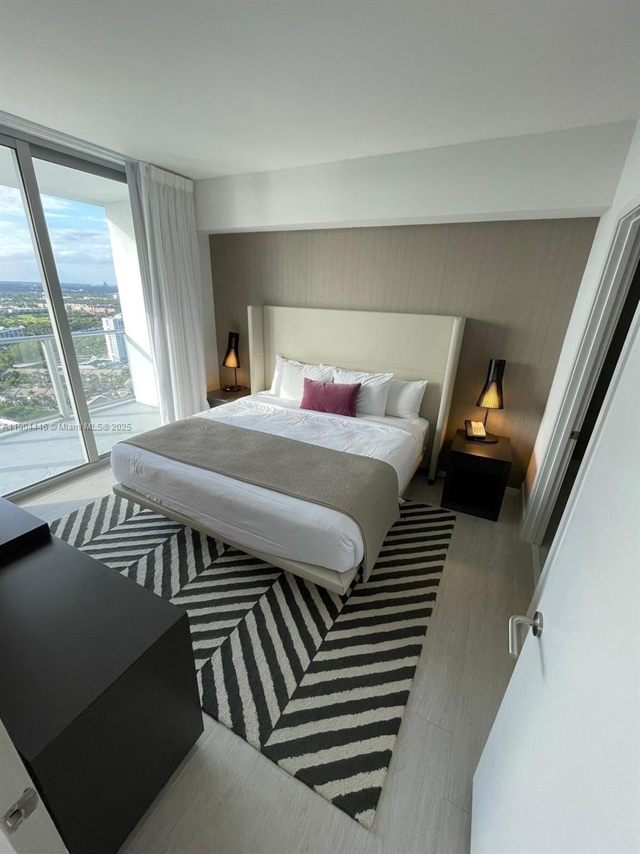 A modern bedroom features a king bed, a geometric rug, and floor-to-ceiling windows with views — 4010 S Ocean Dr # R3306, Hollywood FL 33019, HOLLYWOOD, FL