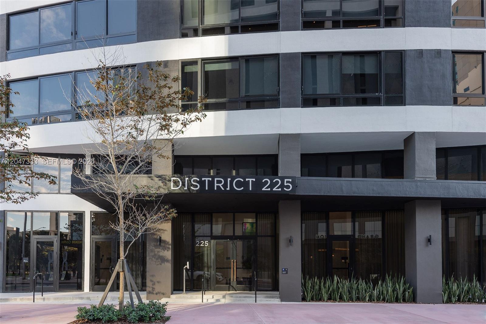 The exterior of a modern multi-story building features a prominent entrance sign reading District 225 — 225 N Miami Ave # 3412, Miami FL 33128, MIAMI, FL