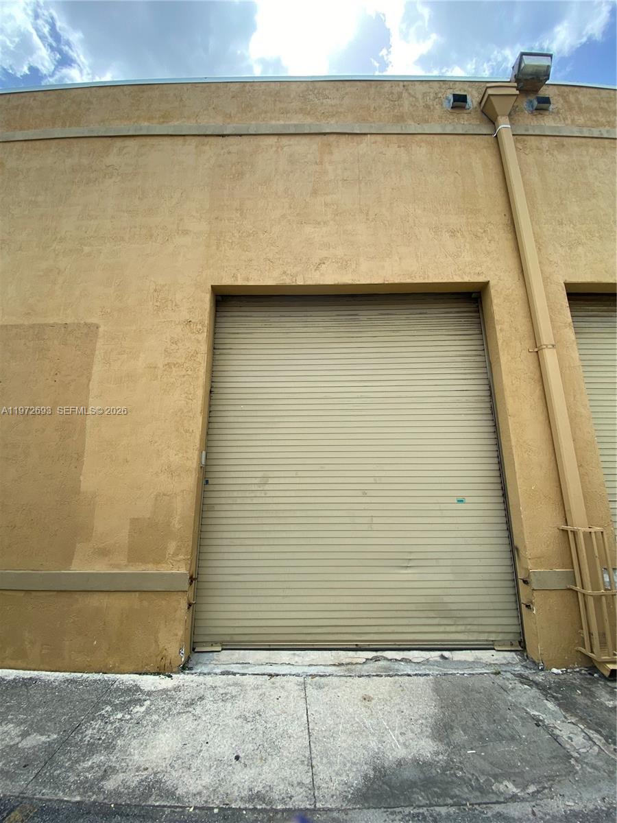 The exterior of a commercial building features a large metal roll-up garage door — 2431 W 80th St # C, Hialeah FL 33016, HIALEAH, FL