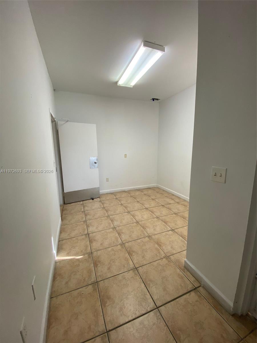 This small, empty room features white walls, tan tile flooring, and a single overhead light — 2431 W 80th St # C, Hialeah FL 33016, HIALEAH, FL