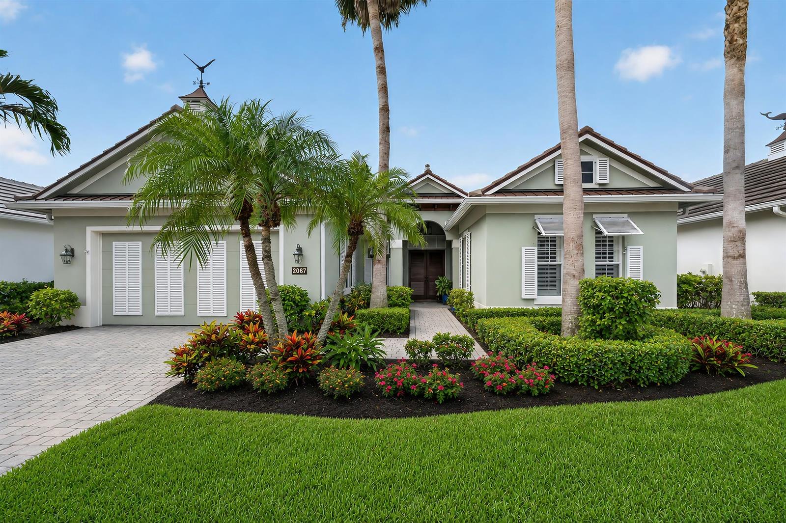 A light green single-story house features a paved driveway, palm trees, and manicured landscaping — VERO BEACH, FL