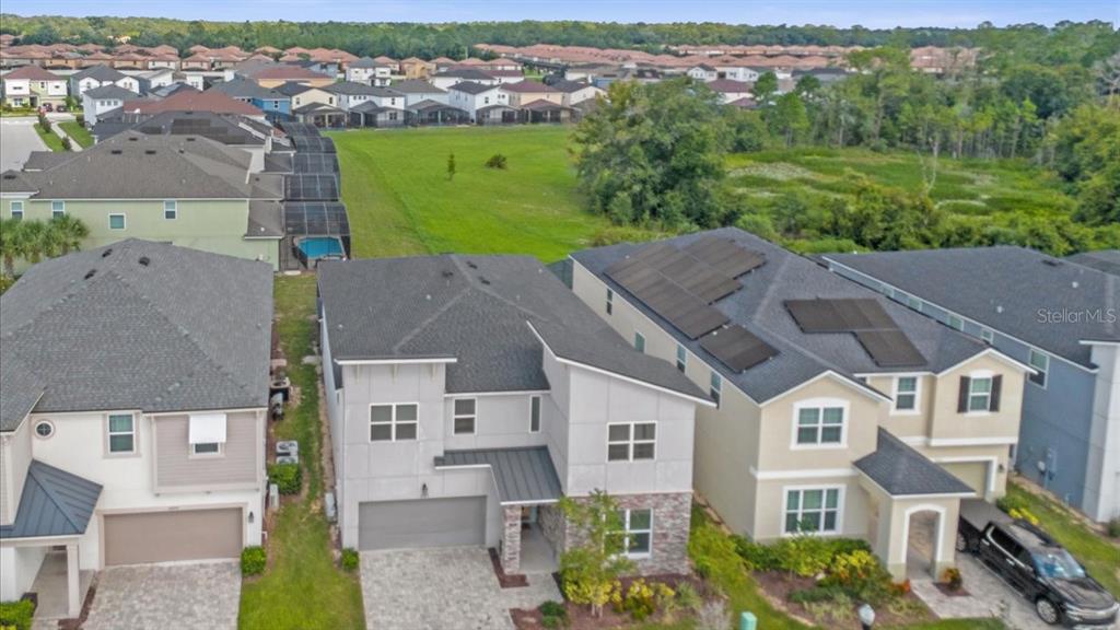 An aerial view shows three suburban houses with paved driveways and a large grassy field — 2089 TROPICAL PALMS CIRCLE, KISSIMMEE, FL
