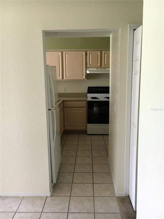 A kitchen with light wood cabinets, white appliances, and tiled flooring viewed through a doorway — 13917 FAIRWAY ISLAND DRIVE UNIT 917, ORLANDO, FL