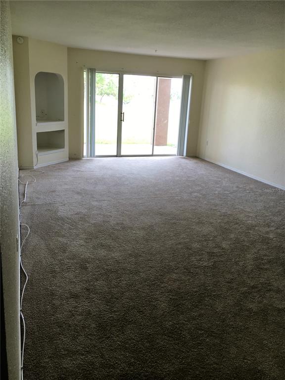 An empty living room features beige carpet, plain walls, and a built-in arched wall niche — 13917 FAIRWAY ISLAND DRIVE UNIT 917, ORLANDO, FL