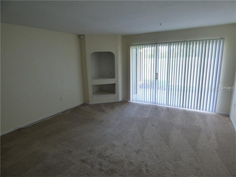 An empty living room features beige carpet, plain walls, a built-in alcove, and sliding glass doors — 13917 FAIRWAY ISLAND DRIVE UNIT 917, ORLANDO, FL