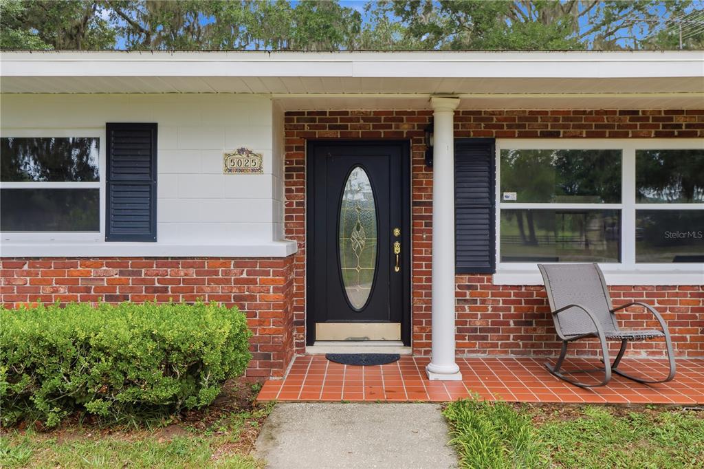 The exterior of a house features a brick facade, a black front door, and a porch — 5025 BASEBALL POND ROAD, BROOKSVILLE, FL