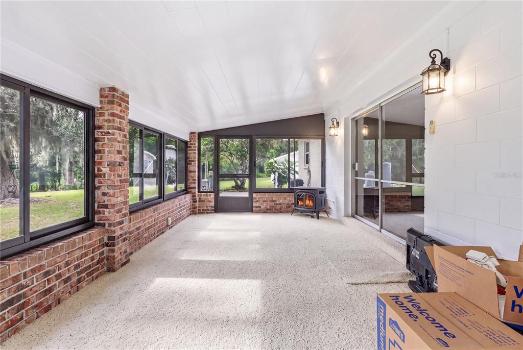 A sunroom features brick walls, large windows, a wood-burning stove, and a white ceiling — 5025 BASEBALL POND ROAD, BROOKSVILLE, FL