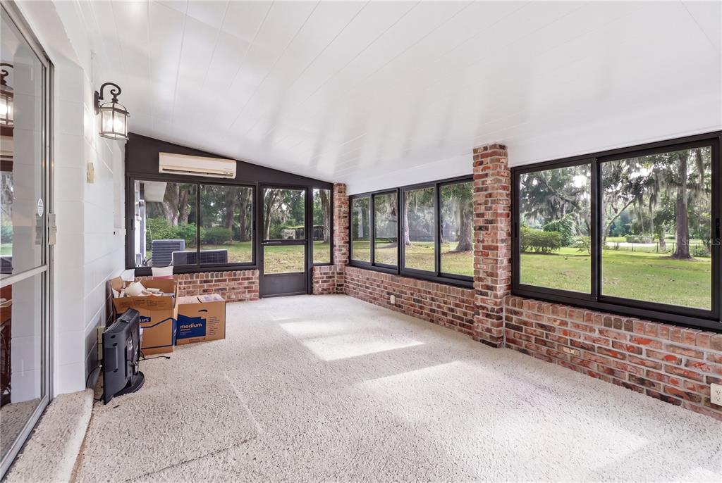 A sunroom features brick walls, large windows, a white ceiling, and carpeted flooring — 5025 BASEBALL POND ROAD, BROOKSVILLE, FL