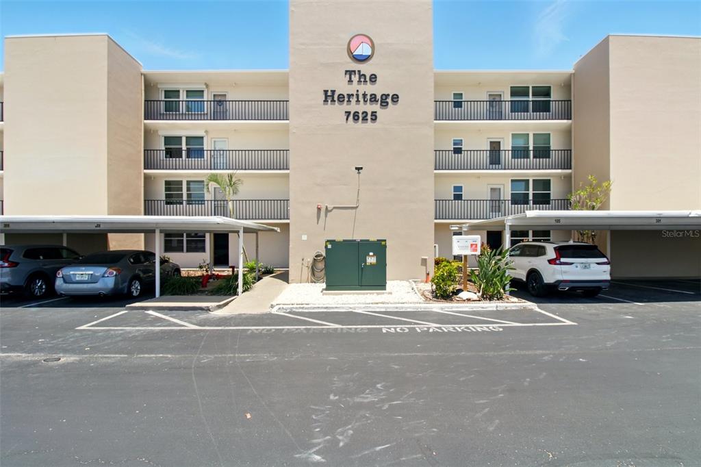 The exterior of a multi-story apartment building features covered parking spaces and a central entrance — 7625 SUN ISLAND DRIVE S UNIT 304, SOUTH PASADENA, FL