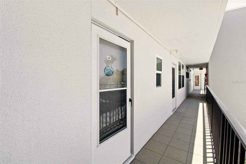 An outdoor apartment building walkway with white walls, tiled floors, and several unit doors — 7625 SUN ISLAND DRIVE S UNIT 304, SOUTH PASADENA, FL