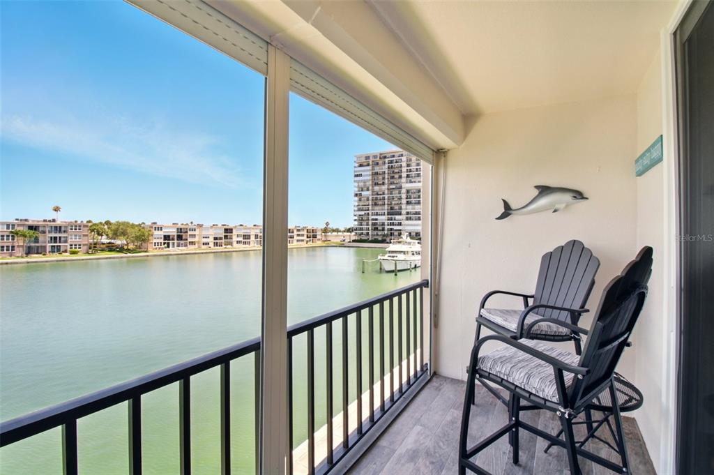A screened-in balcony features two chairs, a dolphin wall decoration, and a water view — 7625 SUN ISLAND DRIVE S UNIT 304, SOUTH PASADENA, FL