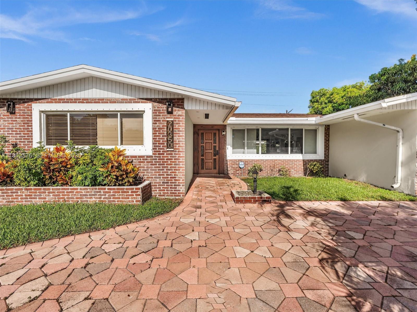 A brick house with a paved driveway and a wooden front door under a roof overhang — 20350 Highland Lakes Blvd, Miami FL 33179, MIAMI, FL