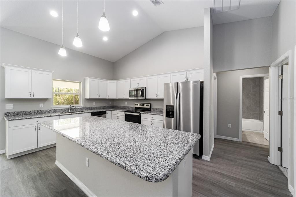 A kitchen features white cabinets, granite countertops, stainless steel appliances, and a large center island — 3617 SW BREEZY POINT DR, DUNNELLON, FL