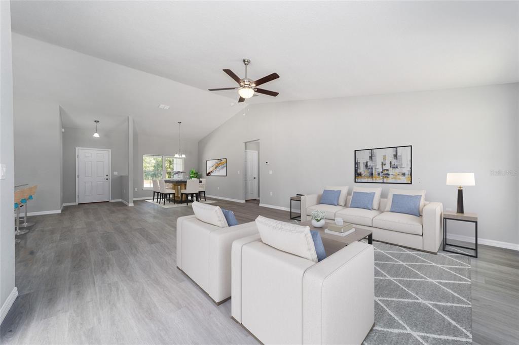 A living room with light wood-look flooring, a vaulted ceiling, and neutral-toned furniture — 3617 SW BREEZY POINT DR, DUNNELLON, FL