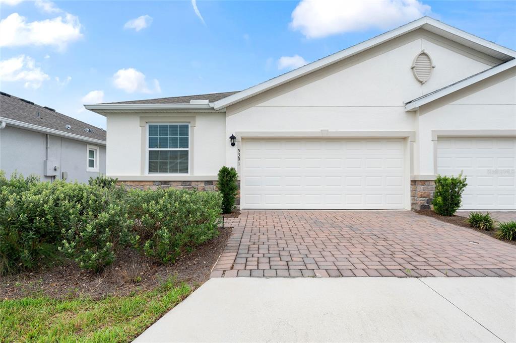 A single-story house exterior features a white stucco facade, a two-car garage, and paver driveway — 5391 NW 46TH LANE ROAD, OCALA, FL