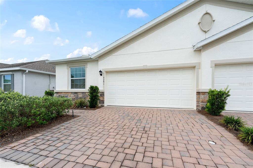 A paved driveway leads to the two-car garage of a single-story home with stucco siding — 5391 NW 46TH LANE ROAD, OCALA, FL