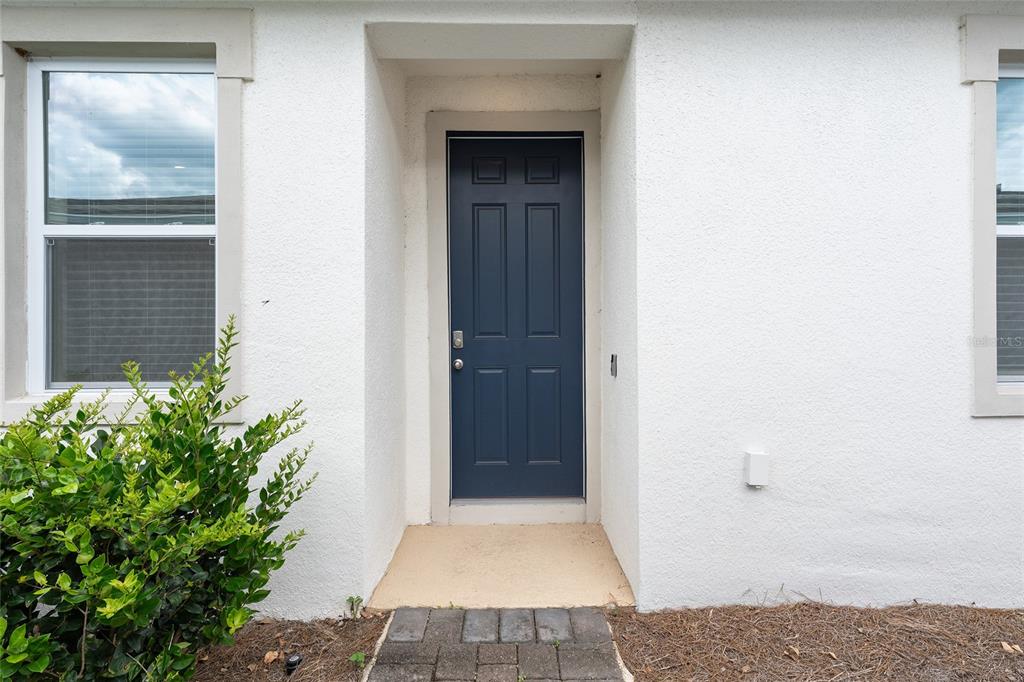 A blue front door is centered on a white stucco exterior wall with a window — 5391 NW 46TH LANE ROAD, OCALA, FL