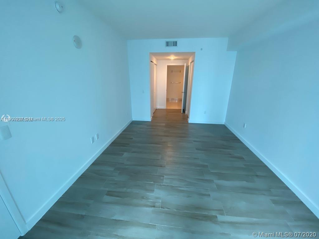 An empty room with light-colored walls and wood-look tile flooring leads to a hallway — 1100 S MIAMI AVE # 3011, Miami FL 33130, MIAMI, FL