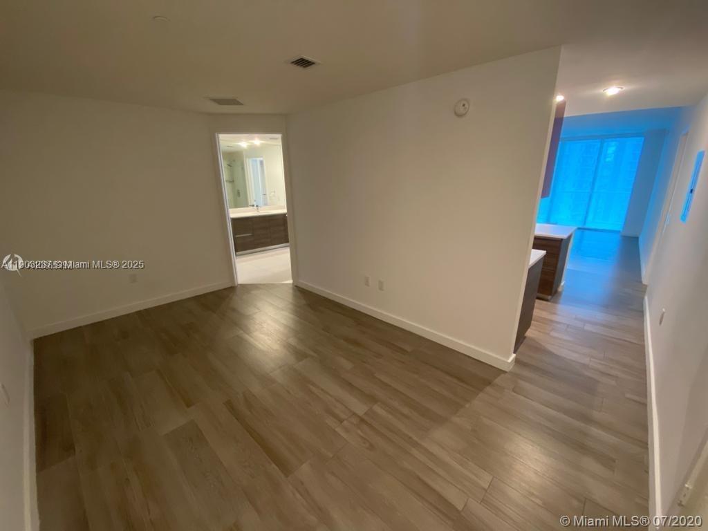 An empty room with wood-look flooring leads to a bathroom and a kitchen area — 1100 S MIAMI AVE # 3011, Miami FL 33130, MIAMI, FL