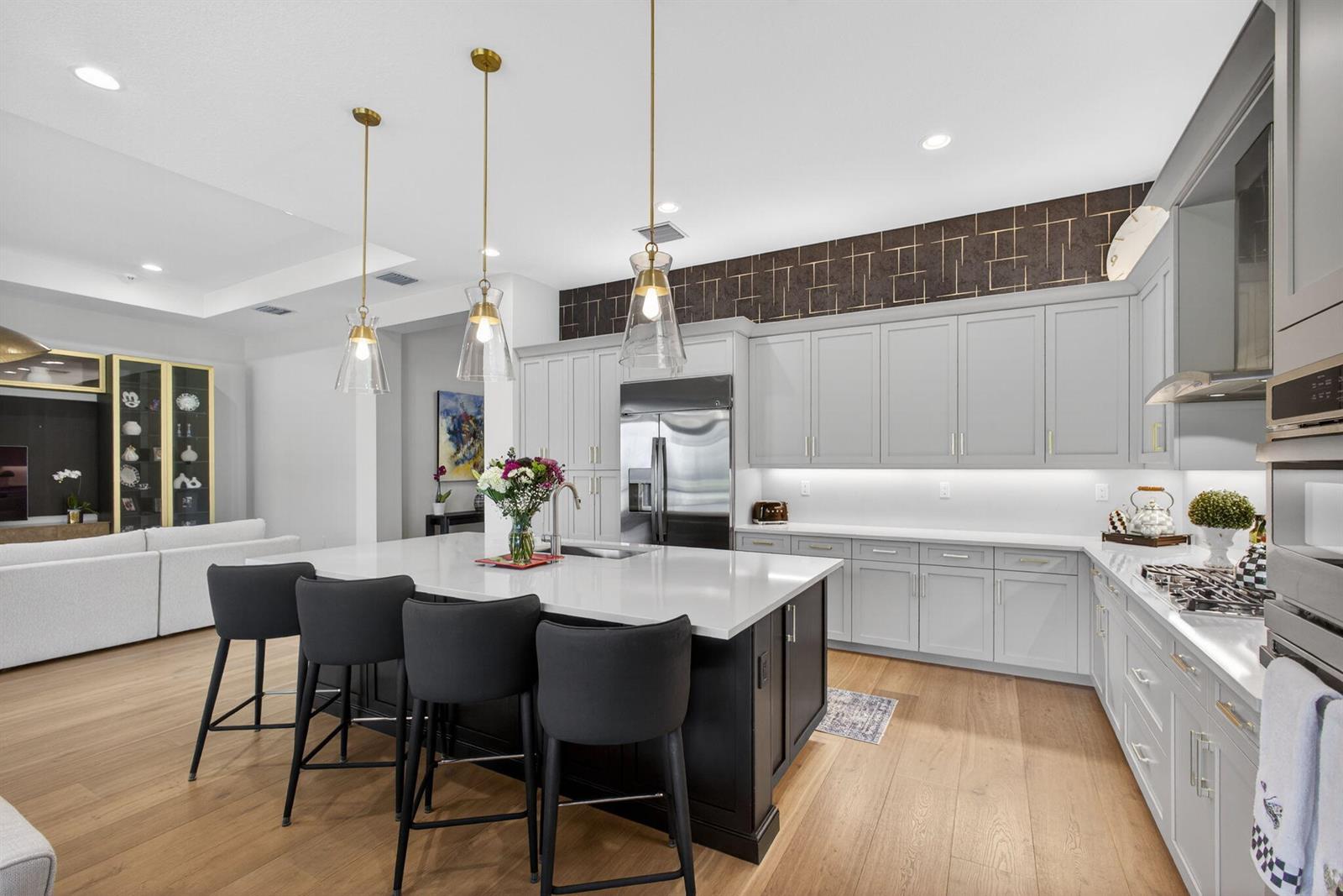 A modern kitchen features a dark island with bar stools, light gray cabinetry, and gold accents — 11104 Glen Orchard Lane, Boynton Beach FL 33473, BOYNTON BEACH, FL