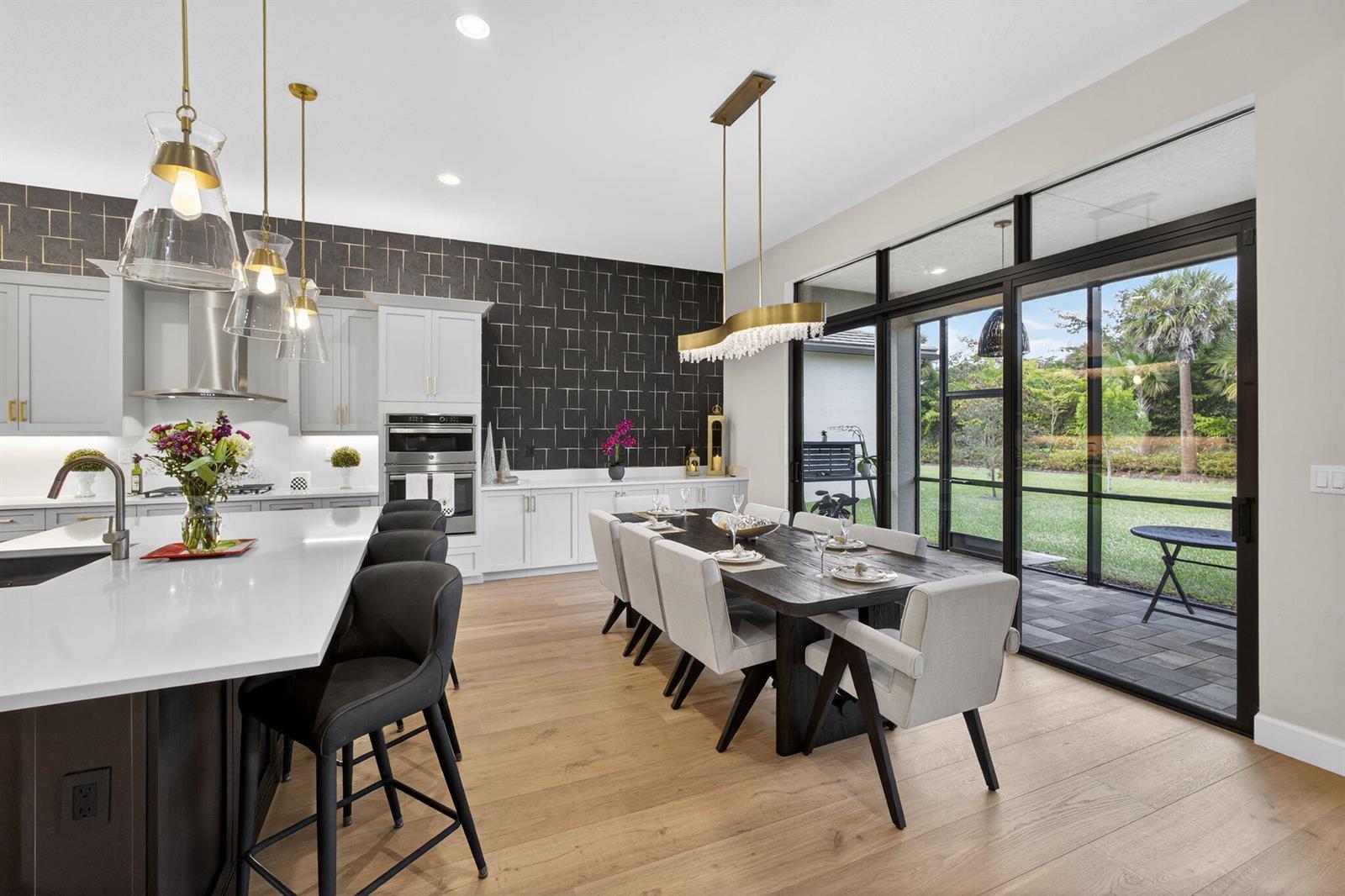 A modern kitchen and dining area features a large island, dark wallpaper, and glass doors — 11104 Glen Orchard Lane, Boynton Beach FL 33473, BOYNTON BEACH, FL