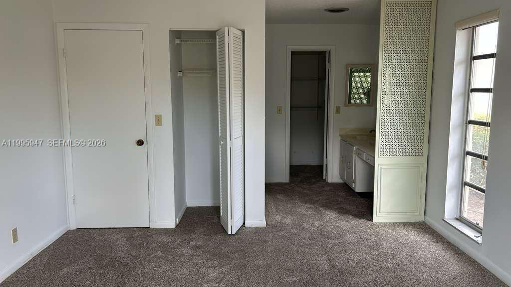 This bedroom features carpeted flooring, a closet, a vanity area, and a window — 13731 Flora Pl # A, Delray Beach FL 33484, DELRAY BEACH, FL