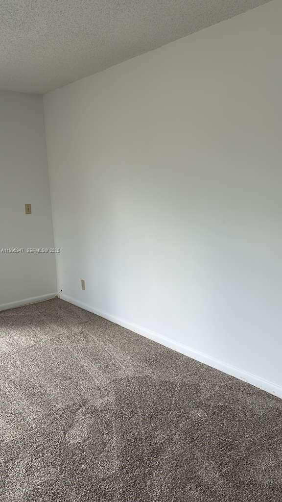 An empty room features white walls, a textured ceiling, and gray wall-to-wall carpeting — 13731 Flora Pl # A, Delray Beach FL 33484, DELRAY BEACH, FL