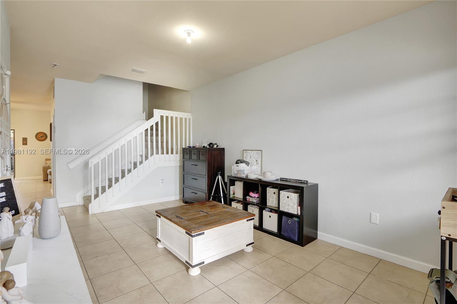 A living room features tile flooring, a staircase with white railings, and dark storage furniture — 338 NE 37th Ave, Homestead FL 33033, HOMESTEAD, FL
