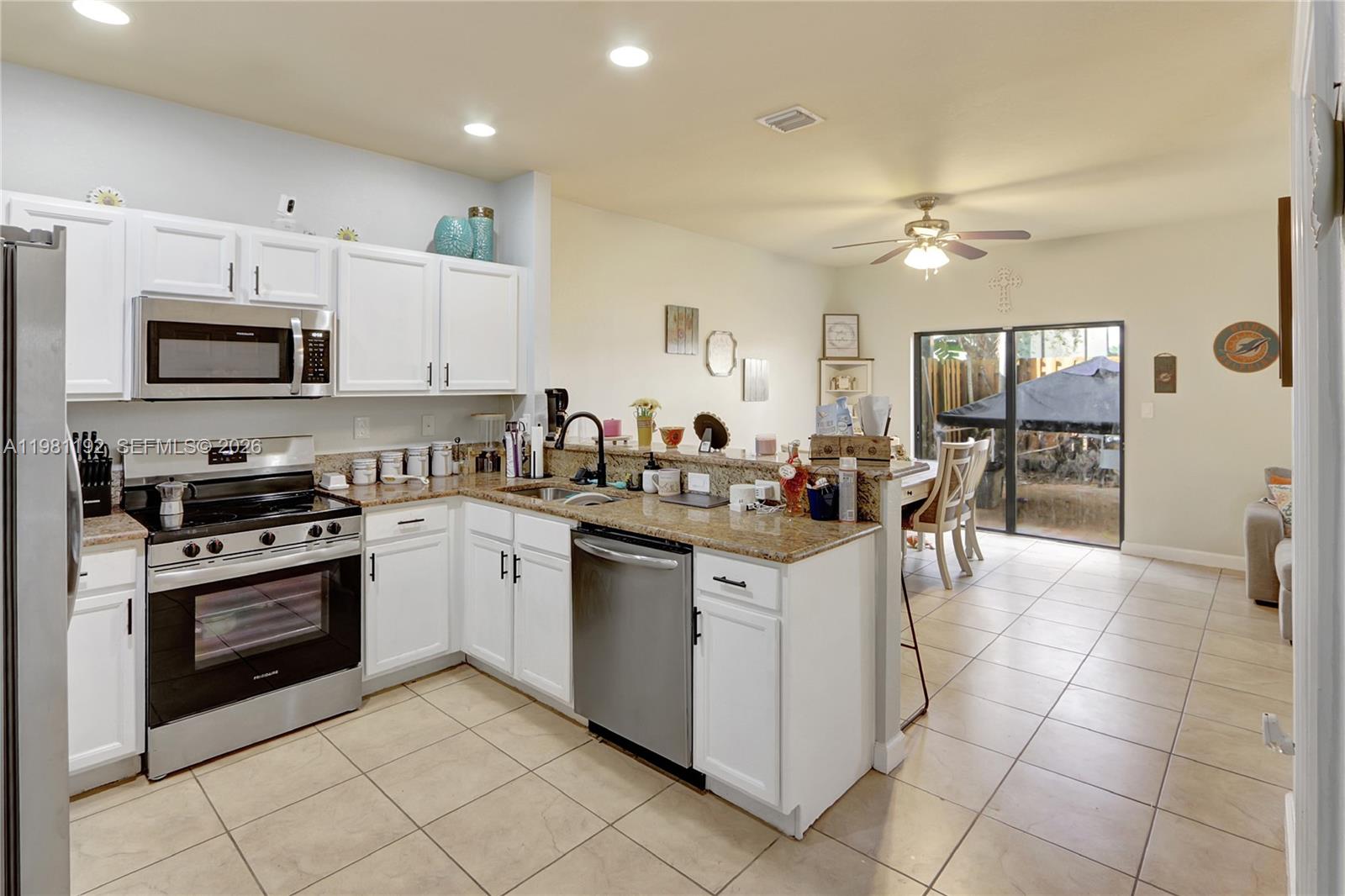A kitchen features white cabinets, granite countertops, stainless steel appliances, and tile flooring — 338 NE 37th Ave, Homestead FL 33033, HOMESTEAD, FL