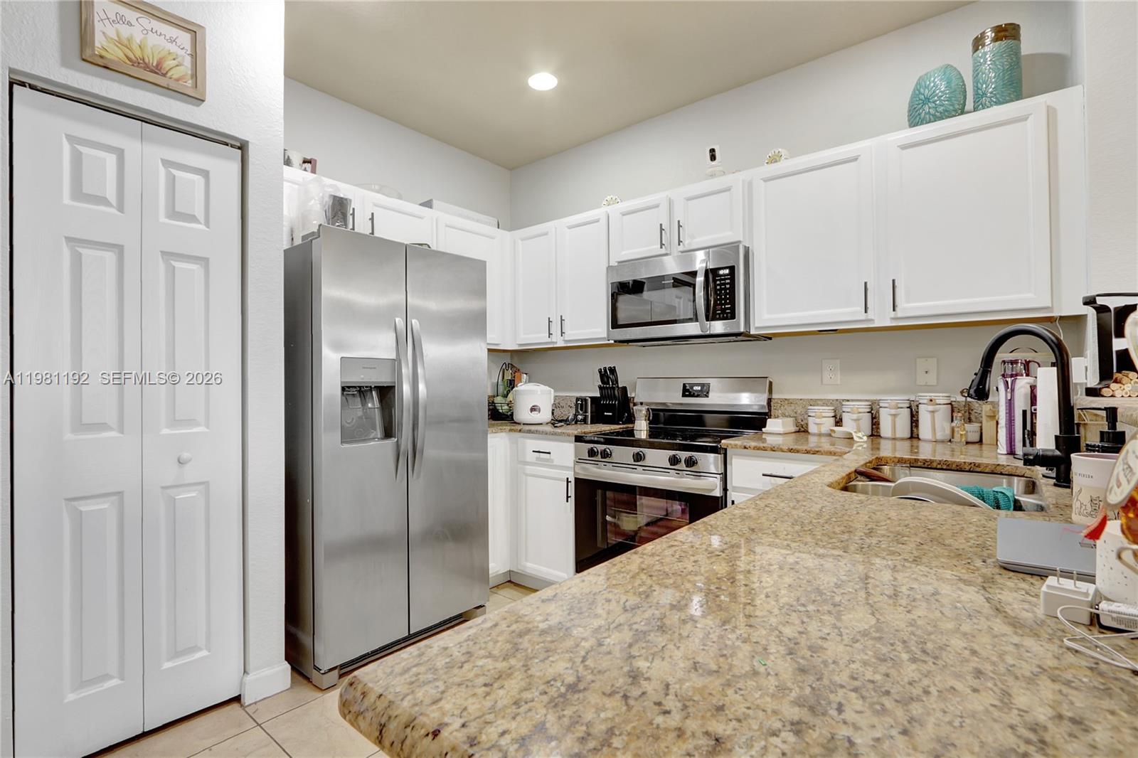 A kitchen features white cabinets, stainless steel appliances, and speckled granite countertops — 338 NE 37th Ave, Homestead FL 33033, HOMESTEAD, FL