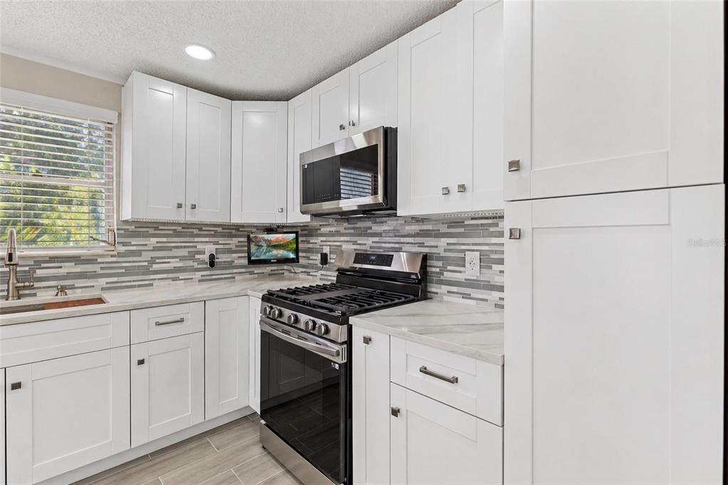 A kitchen features white cabinets, stainless steel appliances, a marble-look countertop, and a tiled backsplash — 5623 80TH STREET N UNIT 316, ST PETERSBURG, FL