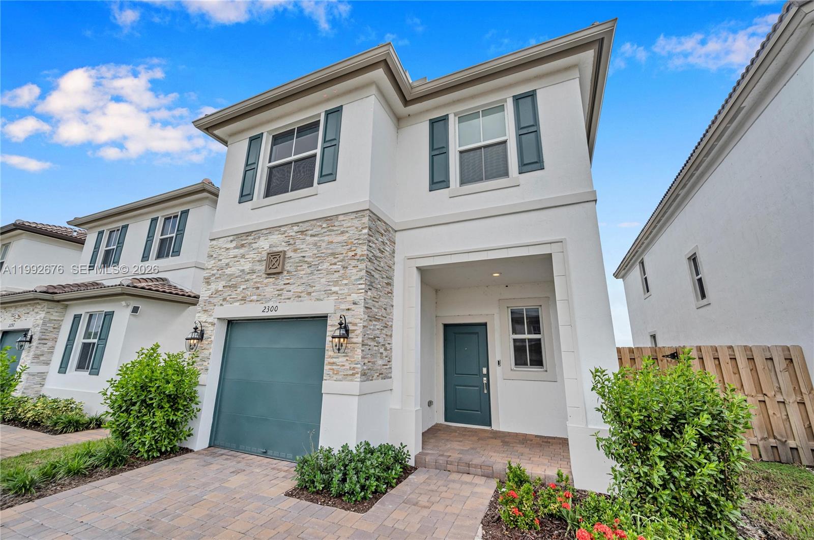 A two-story house features a stone-accented facade, a teal garage door, and a covered entryway — 2300 NW 130th St, Miami FL 33167, MIAMI, FL