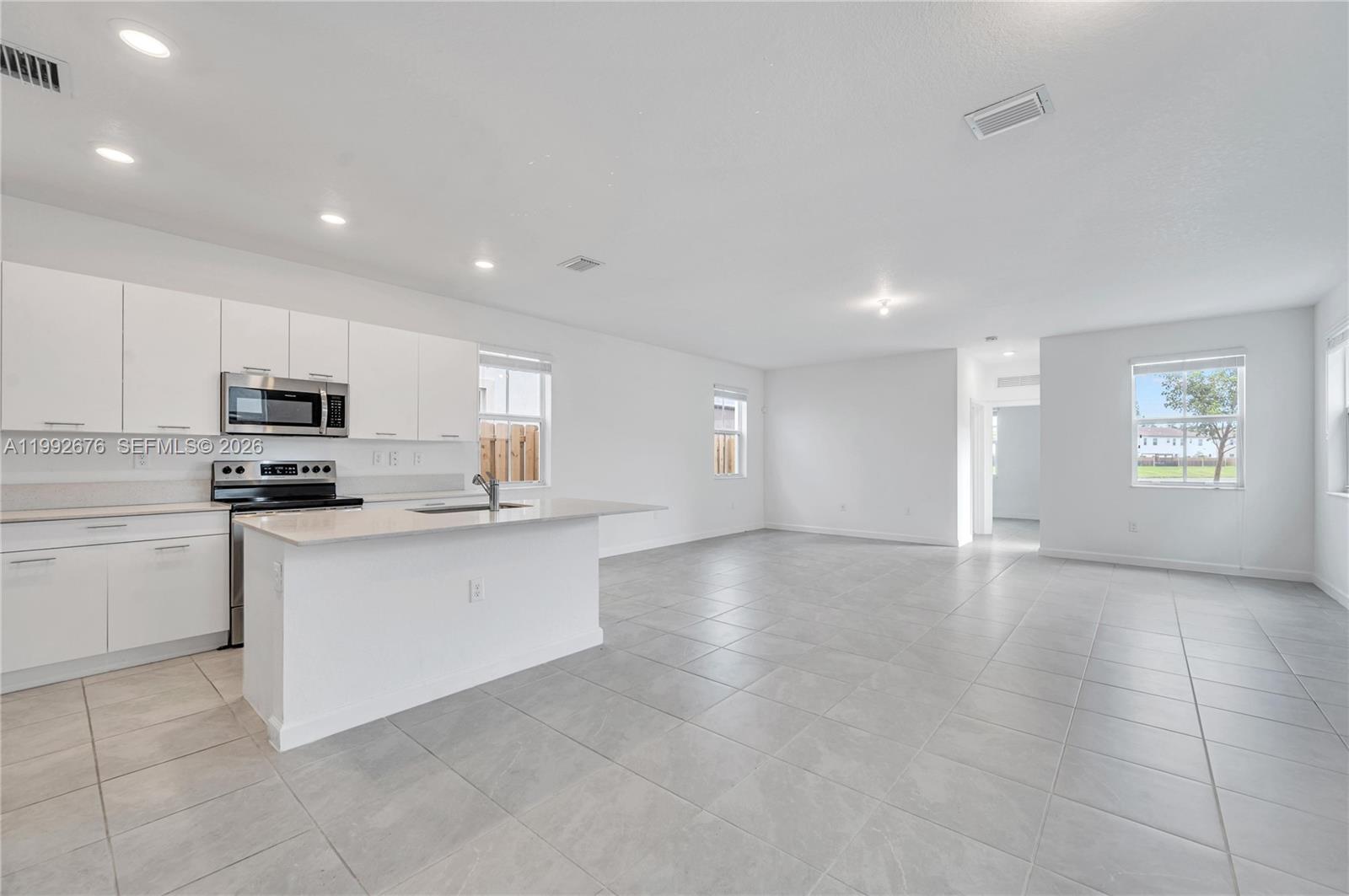 A modern kitchen with white cabinets and a center island opens into a tiled living area — 2300 NW 130th St, Miami FL 33167, MIAMI, FL