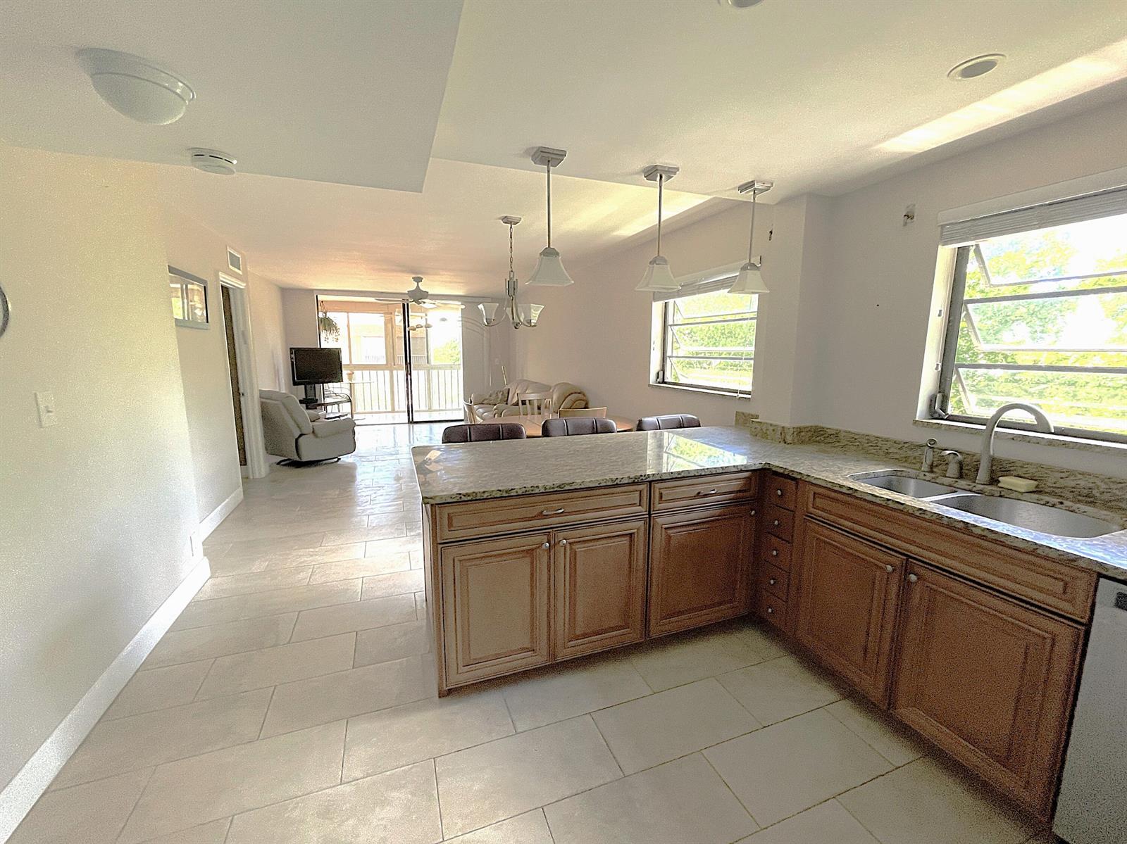 A kitchen with wood cabinets and granite countertops opens into a living area with tile floors — 367 S Federal Highway # C426, Deerfield Beach FL 33441, DEERFIELD BEACH, FL