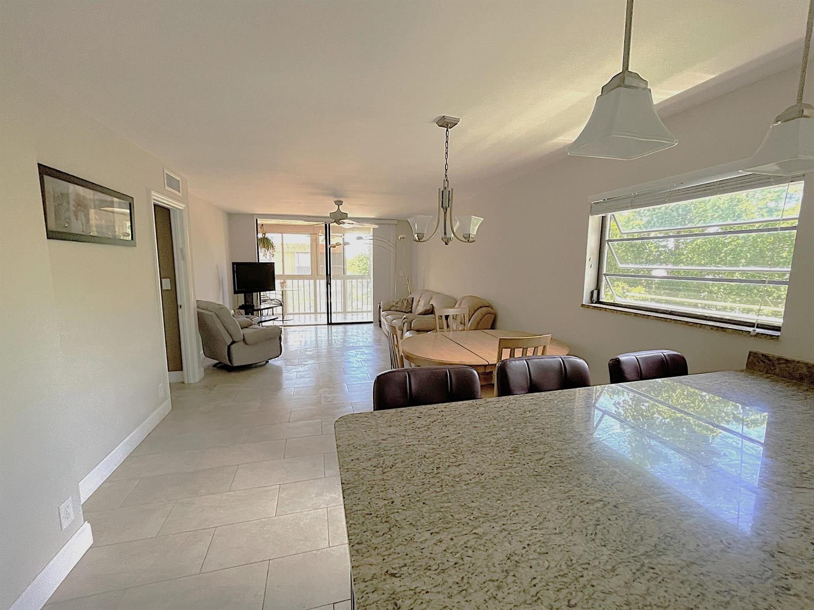 An open-concept living and dining area features tile flooring, a granite countertop, and sliding doors — 367 S Federal Highway # C426, Deerfield Beach FL 33441, DEERFIELD BEACH, FL
